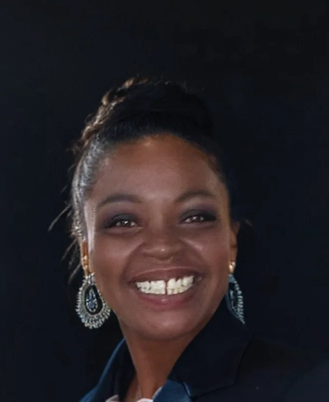 Alissia Matthews, smiling, photographed against a dark background.