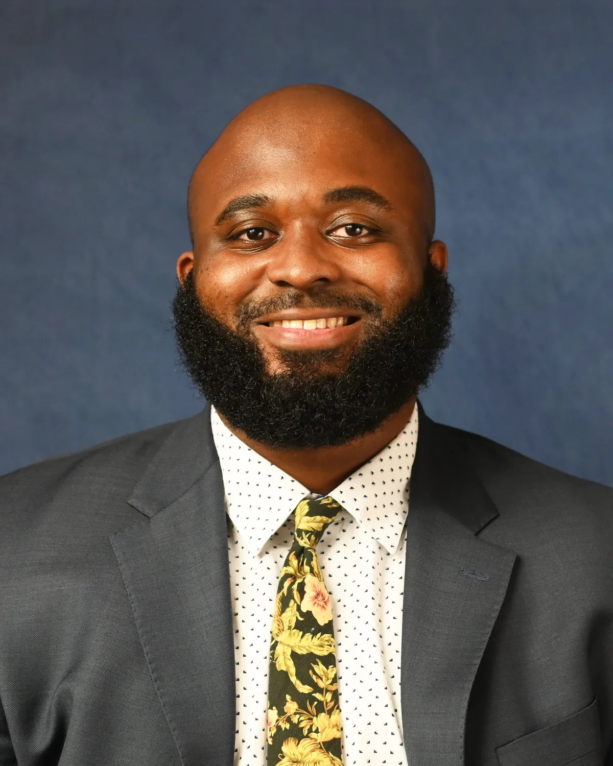 Channing Houser, photographed in a grey suit against a blue studio backdrop.