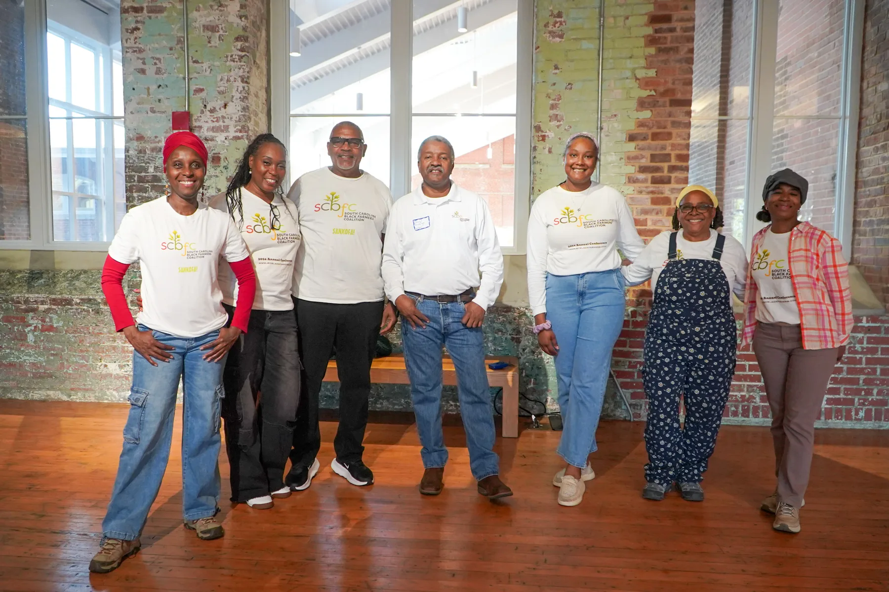 A group stands together for a photograph in a brick-walled hall.