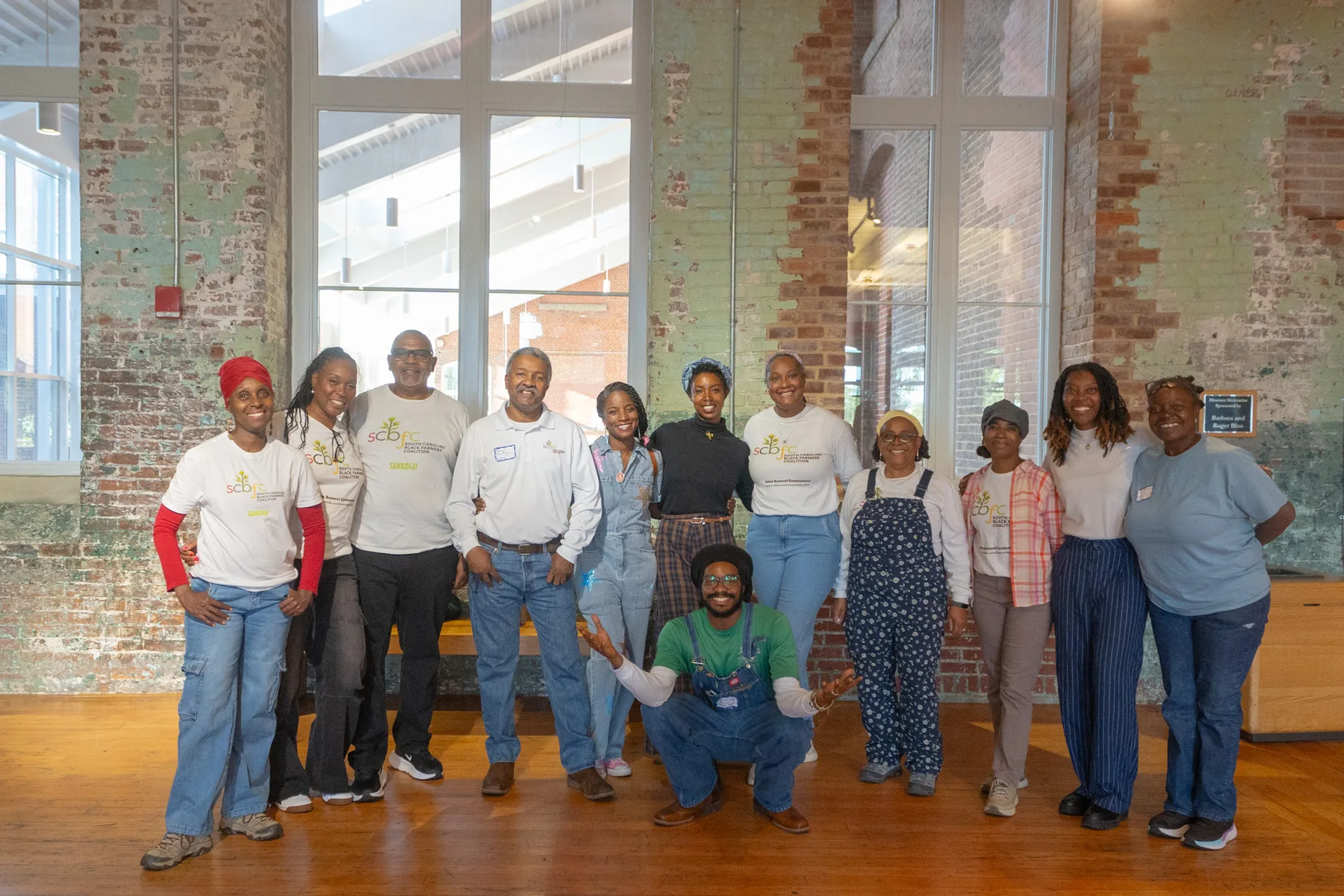 A large group stands together for a photograph in a brick-walled hall.