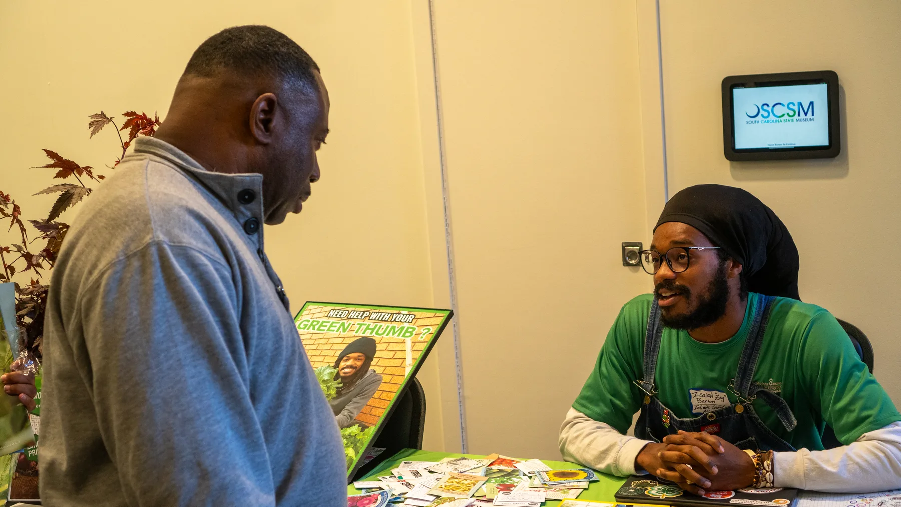 Two people talk across a table spread with printed growing guides.