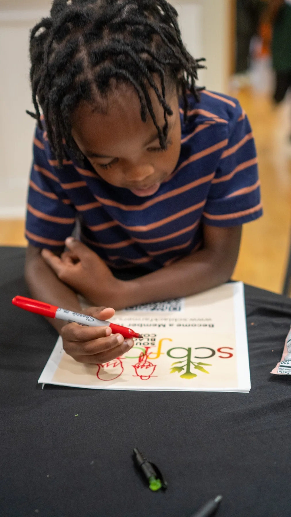 A young person draws with a red marker on a printed activity sheet.
