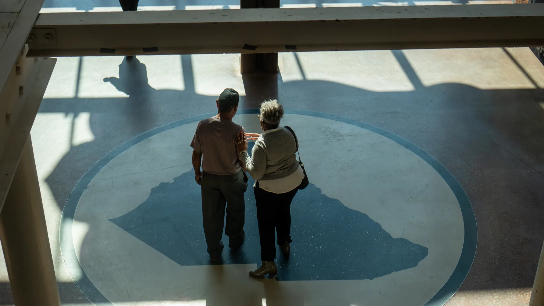 Two people stand on a large floor map of South Carolina.
