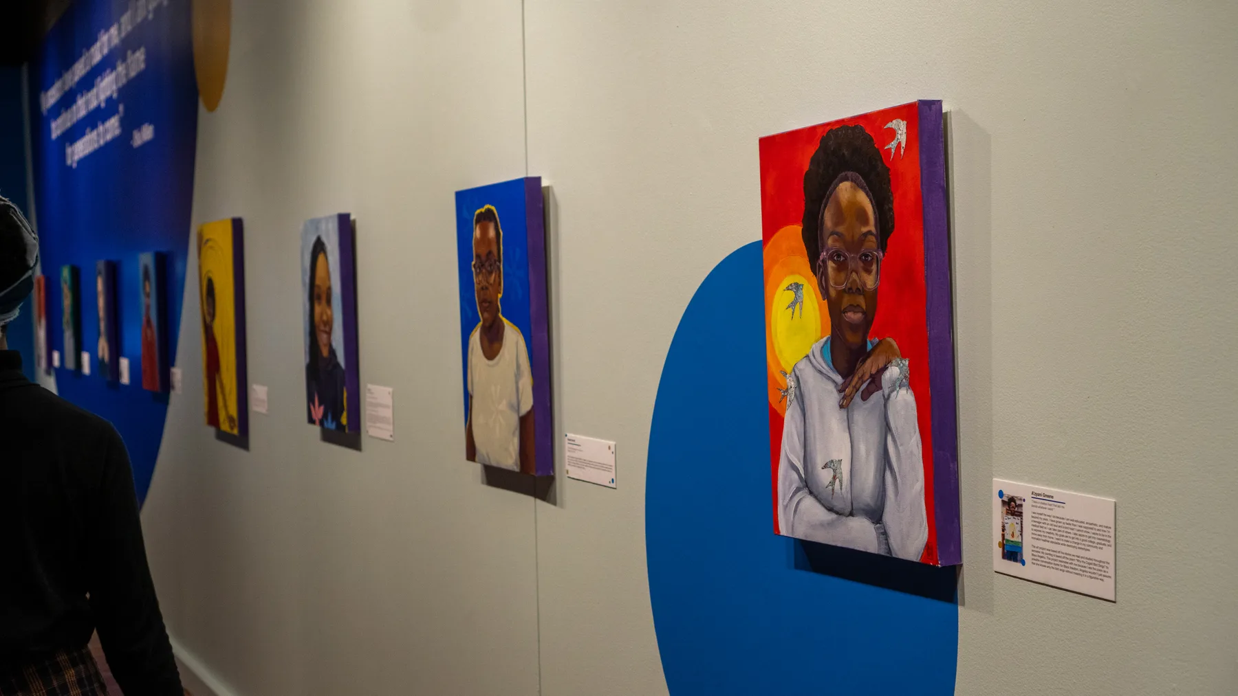 Painted portraits hang along a gallery wall.