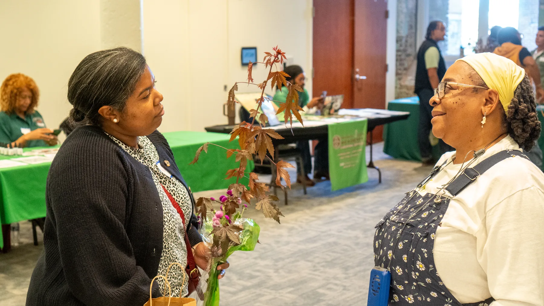 Two people greet each other beside vendor tables.
