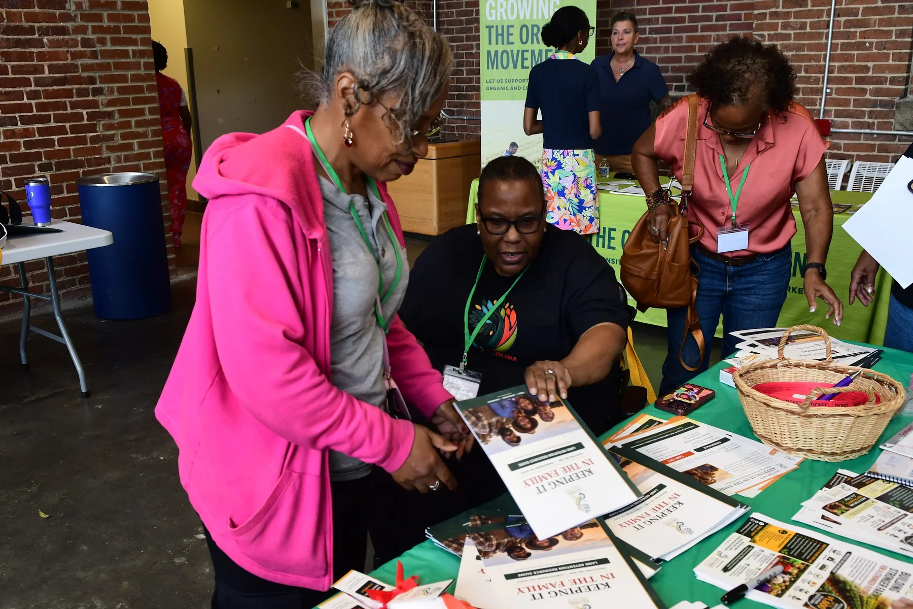 A seated woman shows a visitor in a pink jacket the Keeping It in the Family land-retention resource guide across a table of printed materials.