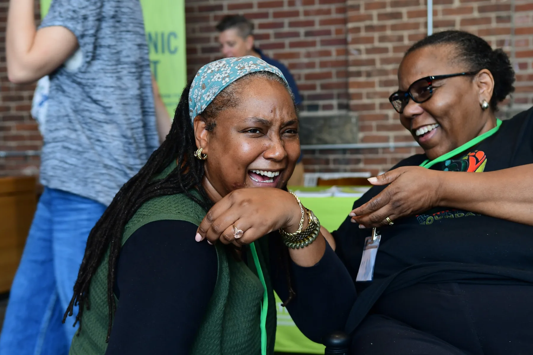 Two women laugh together beside an information table.