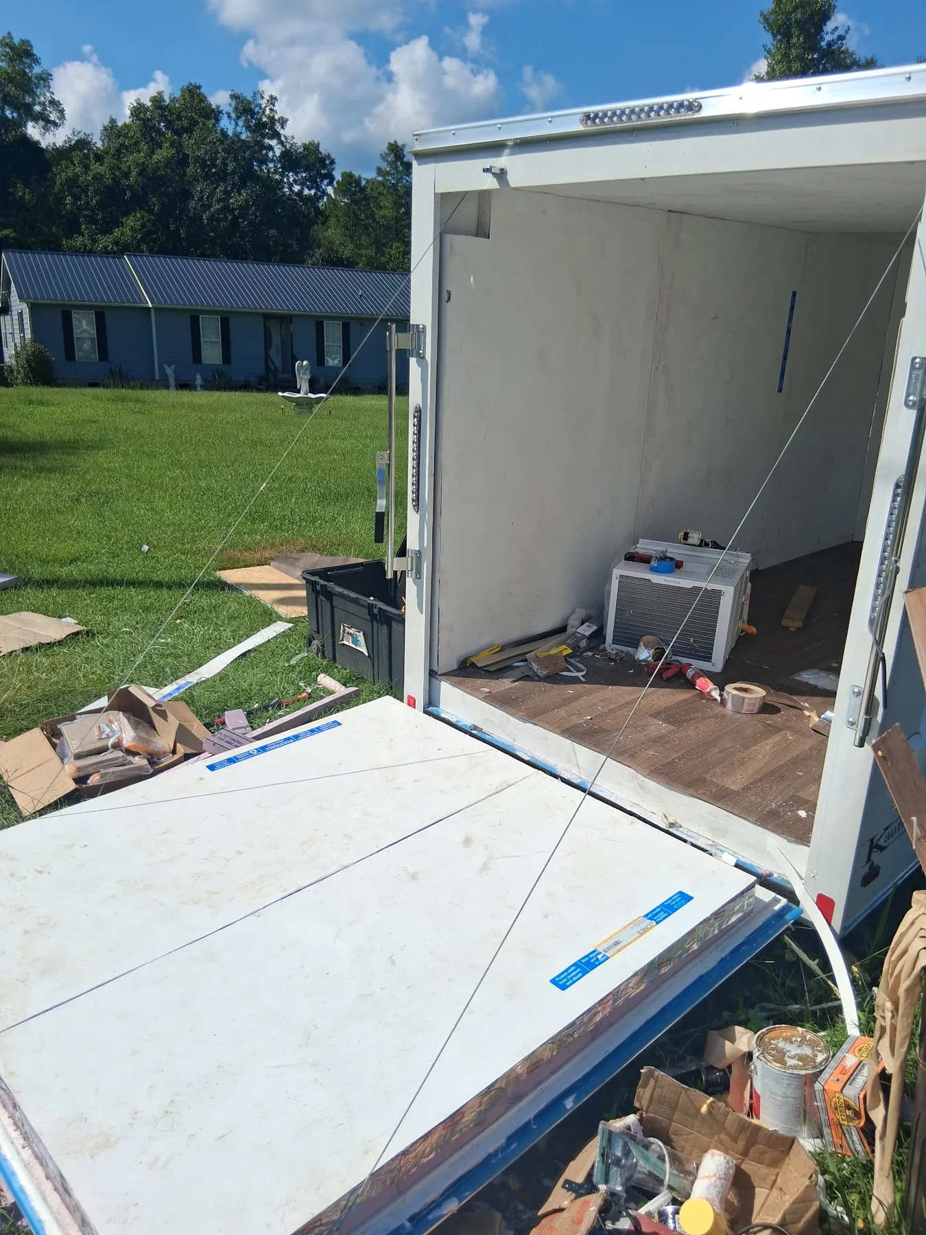 A white mobile cold-storage trailer stands open on a lawn with its cooling unit visible inside.