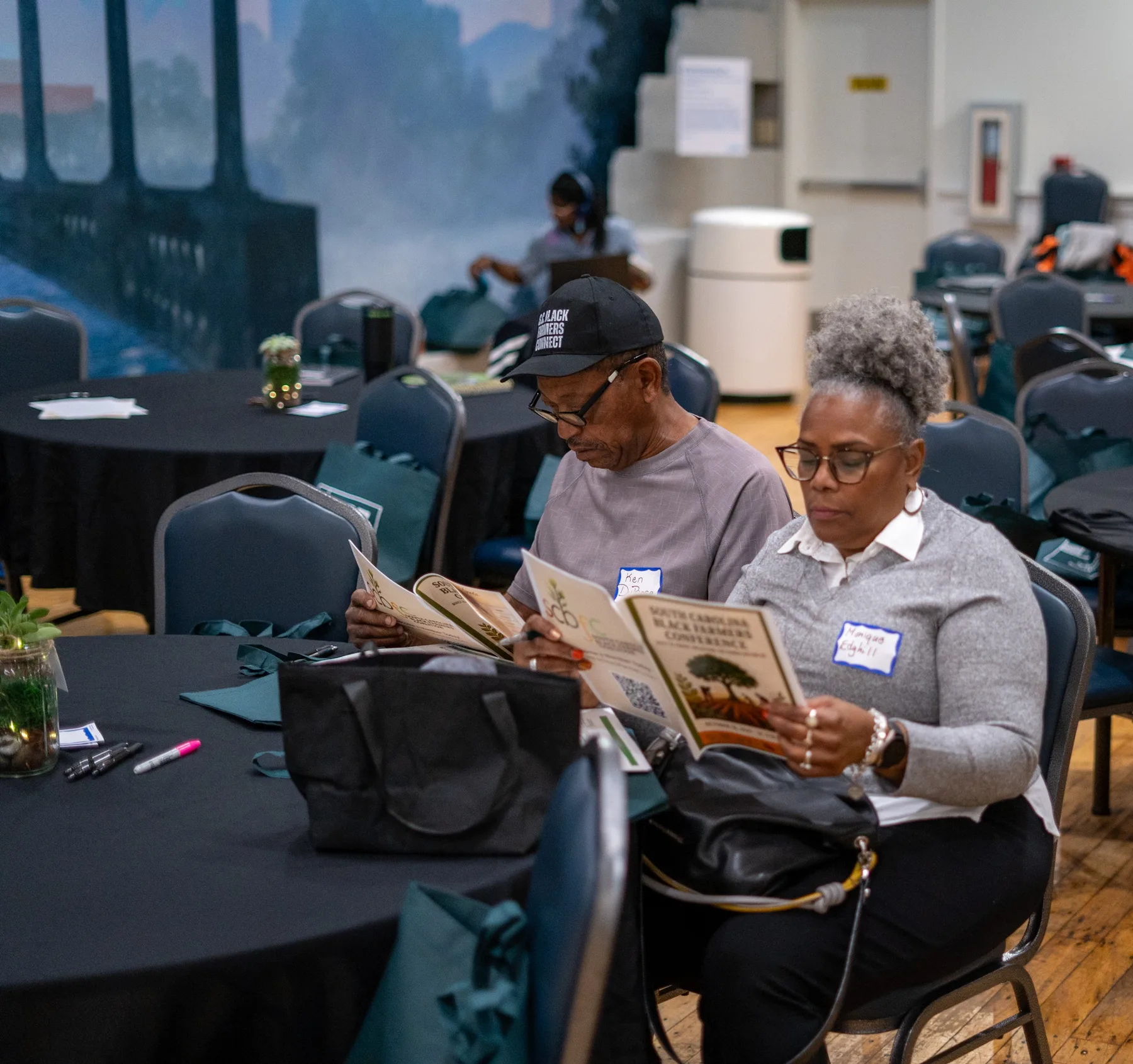 Two people read a printed publication together at a table.