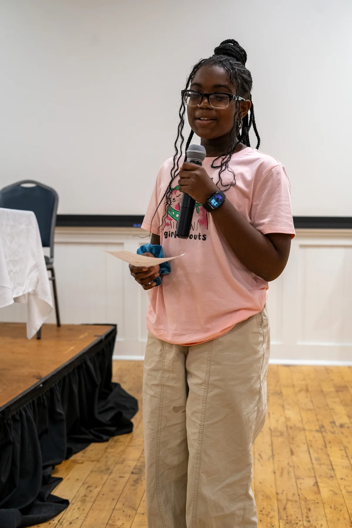 A young person speaks into a microphone at the front of a room.