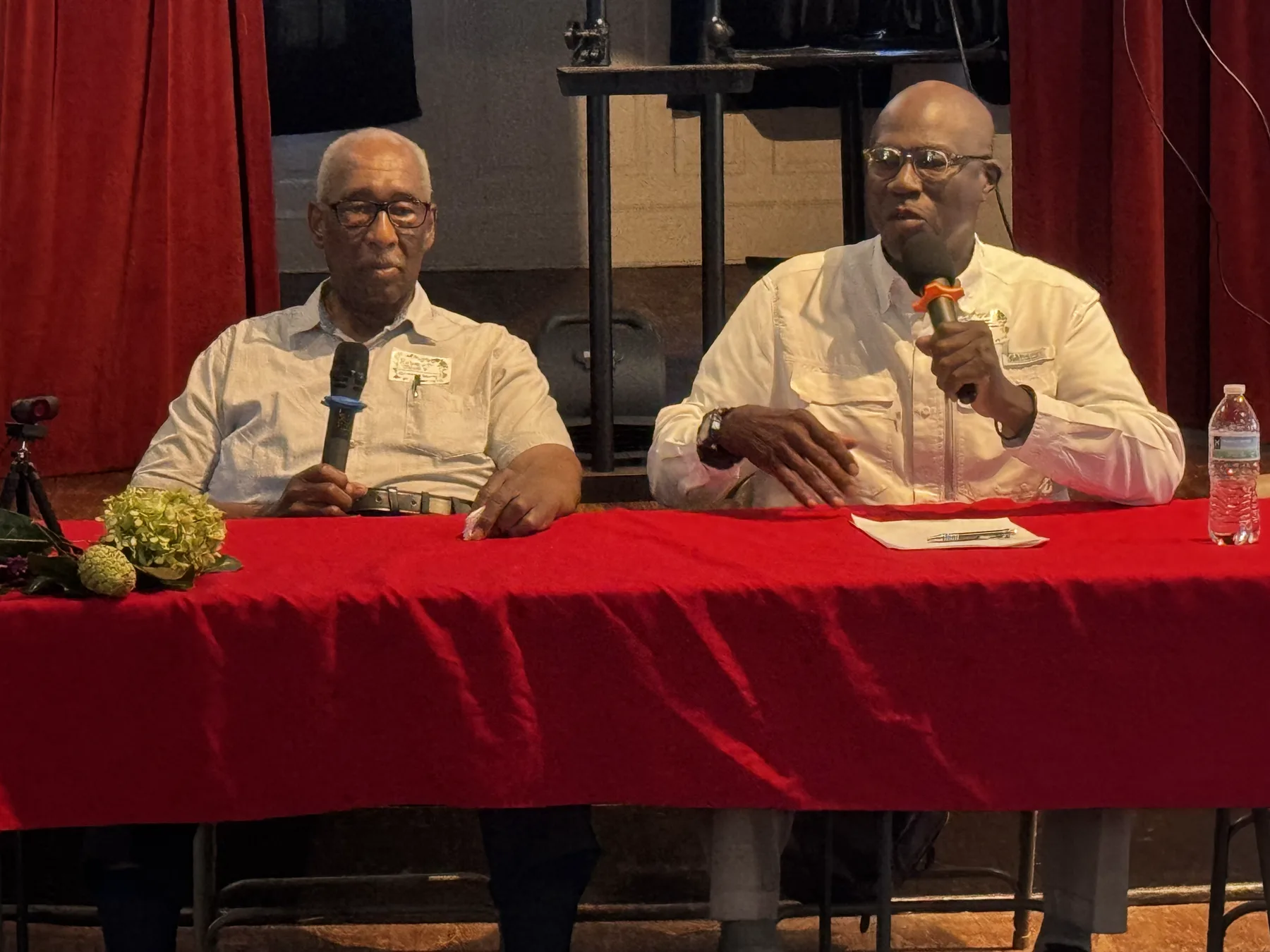 Two panelists with handheld microphones answer questions from behind a red-draped table at Penn Center.